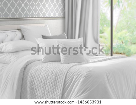 Luxury bedroom that opens with French doors onto a terrace. King bed with white linens and pillows. Interior with garden view window, bed with white bed linen and curtains.