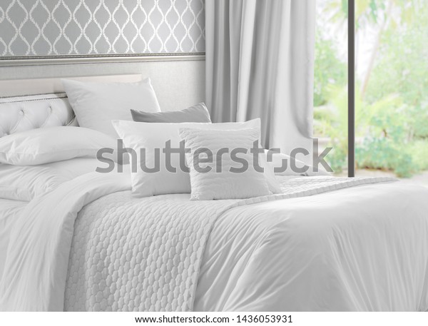 Luxury bedroom that\
opens with French doors onto a terrace. King bed with white linens\
and pillows. Interior with garden view window, bed with white bed\
linen and curtains.
