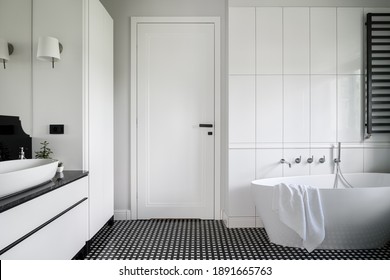 Luxuriöses schwarz-weißes Badezimmer mit freistehender Badewanne, stylischem Mosaikboden und weißen Türen mit schwarzem Griff