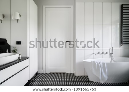 Luxury black and white bathroom with freestanding bathtub, stylish mosaic tile floor and white doors with black handle