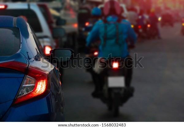 Luxury of blue car stop on the road and open brake\
light. with cars and other motorcycles on the road during heavy\
traffic with orange\
light