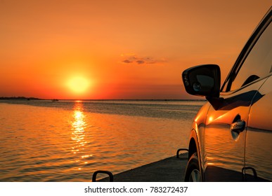 Luxury Blue SUV Car Parked On The Road Beside Tropical Beach With Beautiful Sunset Sky. New Car With Sport And Modern Design. Car Driving For Summer Trip. Automotive Industry. Nature Landscape. 