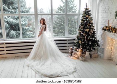 Luxury bride in wedding dress for Christmas near the large panoramic window. Luxury bride in wedding dress for Christmas. Charming bride in an elegant wedding dress. Bride in luxurious suites.