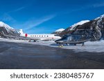 Luxury business jet and helicopter parked at the ramp in the engadin valley in the Swiss alps. The way to travel for the rich and wealthy. Especially in Winter to the ski resort in the mountains. 