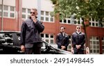 Luxury car business security guard providing VIP protection services, equipped with walkie-talkie, safeguarding high-end client outside corporate event.