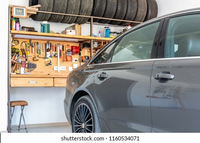 Luxury Car Parked At Large Spacious Private Home Garage. Big Wooden Workbench With Lot Of Tools At Background. Spare Season Wheels Storage. DIY, Self Service And Repair