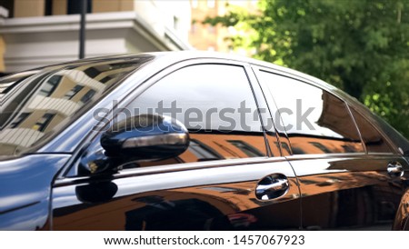 Luxury car with tinted glass standing at parking, reflection of businessman