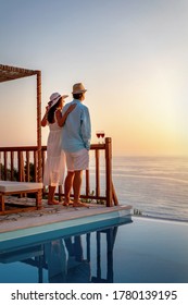 A Luxury Couple In Summer Clothing Stands By The Pool And Is Enjoying The Summer Sunset Over The Ocean With A Glass Of Wine