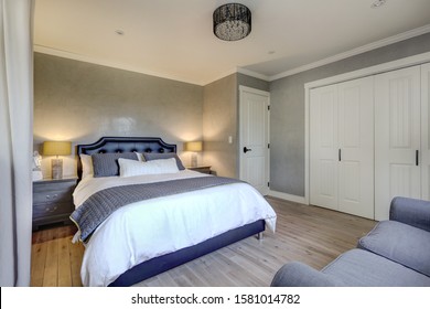 Luxury cozy and elegant guest bedroom with black leather bed frame, white linen with grey blanket and green elements. White doors, like oak floor, and grey sofa and nightstands. Venetian plaster on th - Powered by Shutterstock