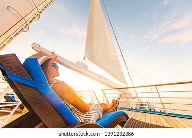 Luxury cruise vacation woman relaxing in lounger chair enjoying sunset on yacht deck with sail in wind sailing in getaway destination summer travel lifestyle.