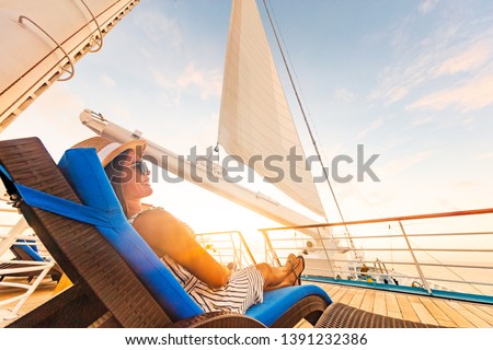 Luxury cruise vacation woman relaxing in lounger chair enjoying sunset on yacht deck with sail in wind sailing in getaway destination summer travel lifestyle.