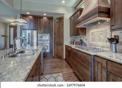 Luxury Dark Wood Rich Kitchen Interior With Copper Stove Hood And Grey Natural Stone Backsplash.