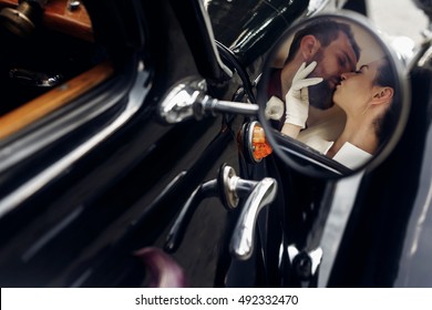 luxury elegant wedding couple kissing and embracing in stylish black car. unusual view in mirror. gorgeous bride and handsome groom in retro style