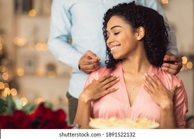 Luxury Gift. Happy African American Woman Receiving Golden Pendant Necklace With Diamond And Bouquet Of Red Roses For Valentine's Day Or Anniversary During Romantic Dinner At Restaurant Or Home