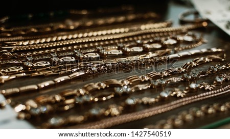 luxury gold jewelry chains, bracelets background, selective focus. Stylish beautiful bijouterie hanging on the stand in the accessories store. Various Jewelry bijouterie.