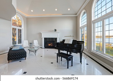 Luxury high ceiling living room features beige ivory walls framing large arched windows, traditional fireplace, black grand piano next to cozy sitting area atop glossy marble floor. Northwest, USA