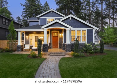 Luxury Home Exterior At Night: Beautiful New House With Green Grass And Landscaping At Twilight.Has Covered Porch And Glowing Interior Lights. 