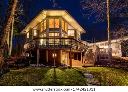 Luxury home with illuminated windows and a large composite deck in the woods.  Photographed at night.  Concepts could include architecture, design, outdoor living, luxury living, nature, others.