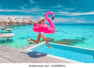 Luxury hotel beach vacation ocean overwater bungalows suite resort. Happy woman tourist jumping of joy in funny pool toy flamingo float excited to be in Bora Bora resort, French Polynesia.