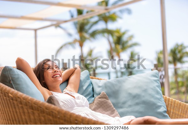 Luxury hotel home living woman relax enjoying sofa\
furniture of outdoor patio. Beautiful young multiracial Asian girl\
relaxing day dreaming for rich early retirement in getaway tropical\
house.