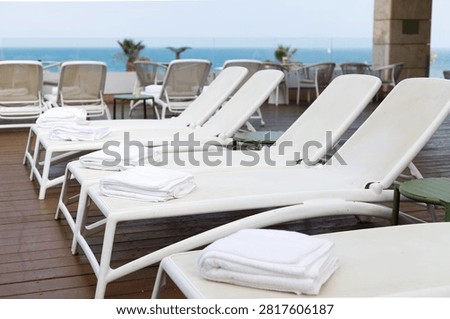 Luxury hotel poolside with white sun loungers and neatly folded towels on a wooden deck, creating an elegant atmosphere for summer vacation, relaxation and resort leisure.