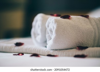 Luxury hotel room with white spa towels on bed sheet with rose petals. Romantic holiday weekend with wellness body treatment  and relax couple massage in honeymoon suite. Closeup.