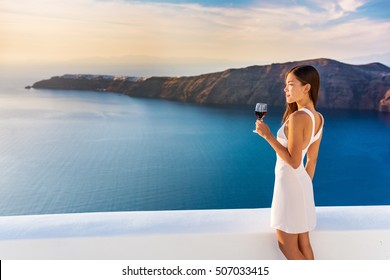 Luxury Hotel Terrace. Europe Destination Summer Vacation. Asian Woman Drinking Red Wine Relaxing Enjoying View Of The Mediterranean Sea In Oia, Santorini, Greece. Honeymoon High End Travel Holiday.