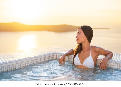 Luxury Hotel Travel Woman In Spa Pool Hotel With Mediterranean Sea Background. Santorini Vacation Summer Holidays Girl Enjoying Holiday Getaway. Asian Model Relaxing.