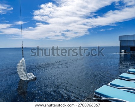 Luxury infinity pool with a hanging wicker swing chair and sun loungers overlooking the calm blue ocean
