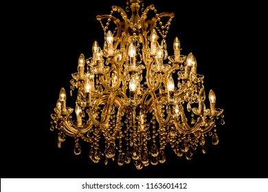 Luxury interior chandelier has light candles and dark background. Noble candelabra hanging on ceiling with lots of little gems. Premium decoration for palace gala, villa business meeting or wedding