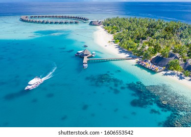 Luxury island landscape in Maldives with boats and perfect blue sea water, palm trees and water villas. Tropical beach as aerial landscape, view from drone. Beautiful nature scenery in Maldives island