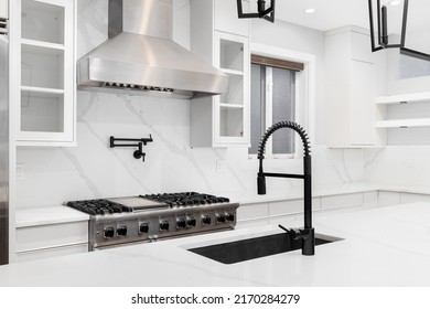 A Luxury Kitchen Detail Shot With A Black Faucet, White Cabinets And Marble Countertops, And Stainless Steel Appliances.