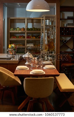 Luxury kitchen dining table setting, glasses, cutlery and wine in ice bucket. Modern kitchen interior with clean white plates, glasses and cutlery on wooden table