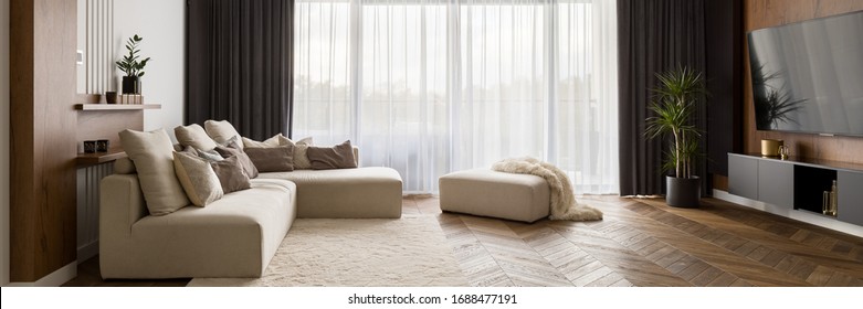 Luxuriöses Wohnzimmer mit großem beigefarbenem Sofa und Holzfußboden und großen Fenstern, Panorama