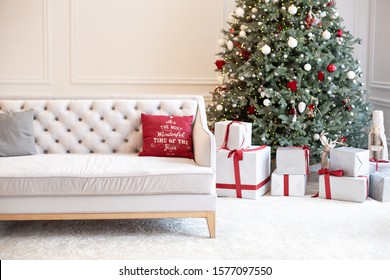 Luxury Living Room Interior With Sofa Decorated Chic Christmas Tree, Gifts And Pillows. Classic Interior In Red Shades. Christmas At Home. Beige Sofa On Background Of Christmas Tree. 
New Year Decor