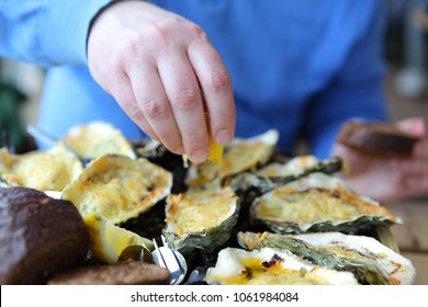 Luxury meal which consists of baked oysters with cheese, bread and lemon, Man squeezing lemon on cooked oyster, mollusk shells macro. Oyster farm in Yerseke, the Netherlands