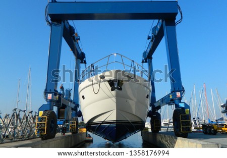 Luxury motor yacht lifted by a special crane for the annual repair, painting and inspection. Transportation industry. Car mechanic. Repair service.
