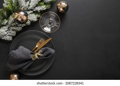 Luxury New Year And Christmas Table Setting With Black Plates, Champagne Flutes, Gold Deer Ring And Gold Cutlery On Black Background With Copy Space. View From Above.