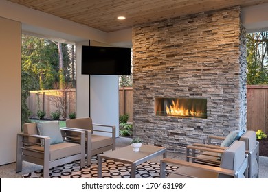 Lujosa sala de estar al aire libre con gran chimenea de piedra, TV, alfombra y sofá beige. 