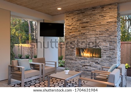 Luxury outdoor relaxing living room with large stone fireplace, TV, rug and beige sofa. 