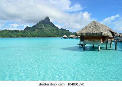 Luxury overwater bungalow with a thatched roof in a honeymoon vacation resort in the clear blue lagoon with a view on Mt. Otemanu on the tropical island of Bora Bora, near Tahiti, in French Polynesia.