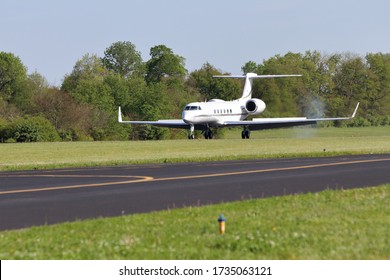 Luxury Private Business Jet Landing At A Small Municipal Airport In Tennessee, USA. Nose Gear Tire Smoke Trails Behind The Plane, Wing Flaps And Spoilers Extended. Heat Mirage Across Wings. 