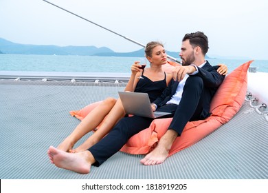 luxury relaxing couple traveler in nice dress and suite sit on bean bag and look at computer in part of cruise yacht with background of sea and white sky. Concept business travel.
