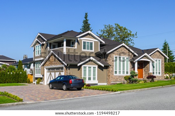Luxury residential house with green hedge on\
side and green lawn in front. Suburban family house with double\
garage and car parked on paved\
driveway