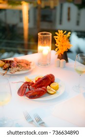 Luxury Romantic Candle Light Dinner Setup By The Pool With Plate Of Lobster And Seafood BBQ