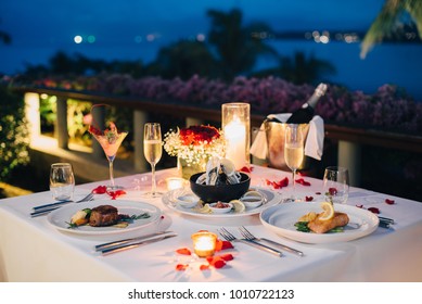 Luxury Romantic Candlelight Dinner Table Setup For Couple In Ocean View Restaurant On Valentine's Day With Champaign & Wine Glasses And Beautiful Food Decoration.  