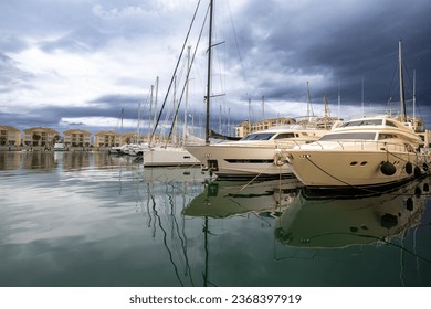 Luxury sailing boats moored in the Gibraltar marina, reflecting in the water with dark storm clouds looming in the background. - Powered by Shutterstock