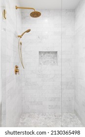 A luxury shower with a gold faucet and shower head, marble subway tile walls, and marble hexagon tile shelf and floor.