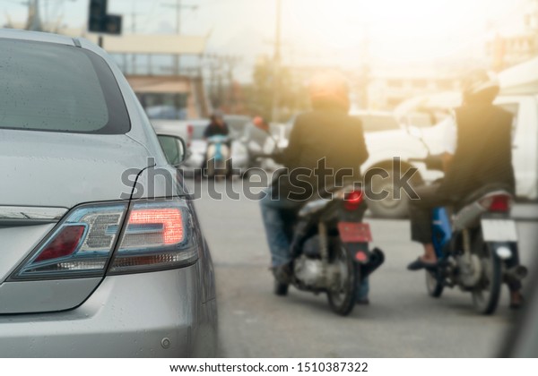 Luxury of silver car stop on the asphalt road. Stop\
by traffic red light control in across. Traveling in the provinces\
during the bright period. Open light brake. With Motorcycles and\
other cars.