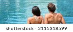 Luxury spa couple relaxing at swimming pool resort panoramic. Adults only hotel travel vacation honeymoon getaway. Woman and man relaxation concept. Two people from behind enjoying summer holidays